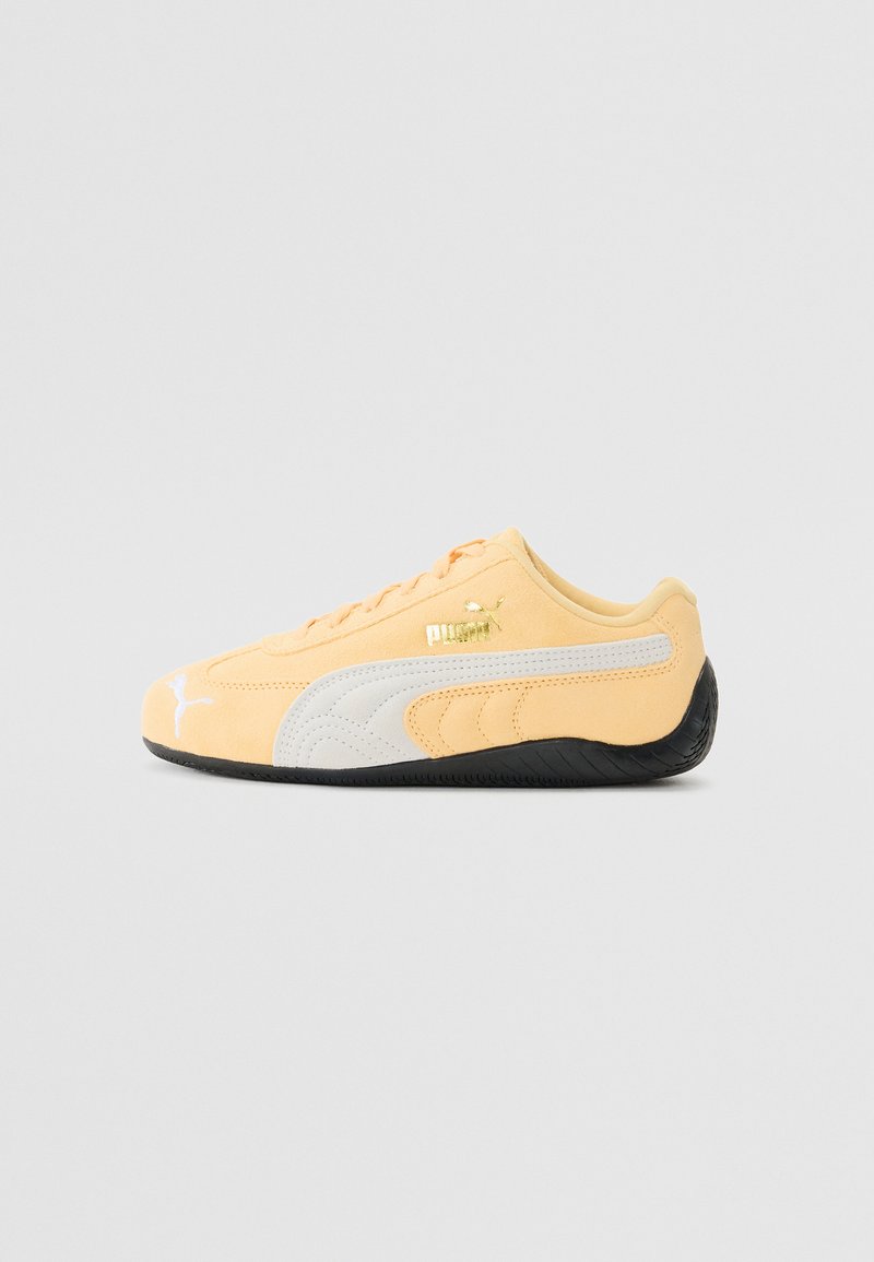 Yellow suede sneaker with white accents and black rubber sole. Features a curved design and embroidered logo on the side.