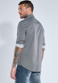 Grau gemustertes Hemd mit Button-Down-Kragen und hochgekrempelten Ärmeln, das eine subtile Textur und einen geraden Schnitt aufweist, kombiniert mit blauen Jeans.
