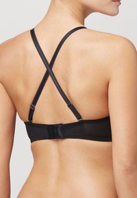 Zwarte bh met gekruiste bandjes, gemaakt van gladde stof, voorzien van haakjes voor sluiting en delicate randafwerking langs de band.