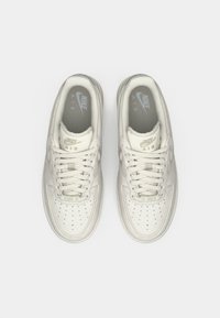 Sapatilhas de couro branco com caixa de dedos perfurada, atacadores e colarinho acolchoado. Marcação "Nike Air" na língua e na palmilha, textura suave.