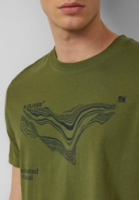 Olijfgroen T-shirt van katoen, met een zwarte golvende lijn en tekst. Ronde hals en korte mouwen. Casual pasvorm.