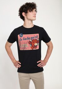 Černé bavlněné tričko s barevnou vintage ilustrací krávy, na které je text "La Vache qui rit" a detail kruhového loga.