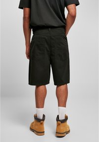 Sorte shorts med en afslappet pasform, lommer bagpå, sammen med brune arbejdssko og hvide sokker. Glat tekstur, afslappet design.