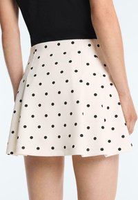 Jupe crème évasée à taille haute avec des pois noirs espacés uniformément, portée avec un haut noir, vue de dos.