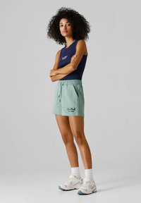 Jasnozielone spodenki z elastycznym pasem, z boczną kieszenią i nadrukiem "Red Bull Racing" w ciemnoniebieskim kolorze. Połączone z granatowym topem na ramiączkach.