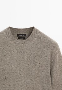 Maglione grigio in lana con scollo rotondo, caratterizzato da una texture screziata e colletto a coste. Etichetta del brand visibile all'interno della zona del collo.