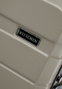 Béžový tvrdý kufr s texturovaným povrchem, vybavený černou značkovou destičkou s nápisem "WITTCHEN" a elegantním designem pro odolnost.