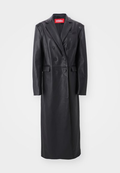 Zwarte leren dubbelbreasted jas, lange lengte, met klepels, zijzakken, gestructureerde afwerking, met een zichtbaar rood merklabel bij de kraag.