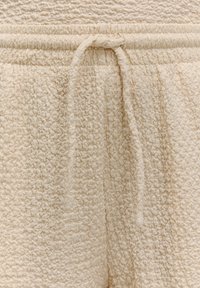 Beige textuur broek van een zachte, lussenstof, met een elastische tailleband en een trekkoord voor een verstelbare pasvorm.