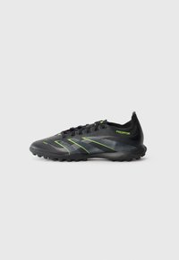 Chaussure de football noire et grise avec des accents vert fluo, des lacets et une semelle texturée conçue pour une utilisation sur gazon ou sol ferme.