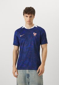 Maglietta da calcio blu navy con design testurizzato, colletto bianco e accenti rosa. Presenta un logo di gallo e il marchio Nike sul petto.