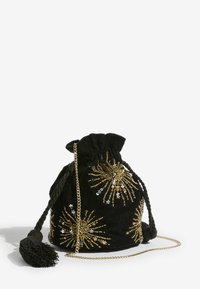 Čierna zamatová taška so sťahovacou šnúrkou a zlatými korálkami usporiadanými do vzorov pripomínajúcich hviezdny výbuch, vybavená zlatým reťazovým remienkom a čiernou strapcovou ozdobou.