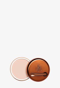 Compact en bronze avec une crème lisse et rose à l'intérieur. Le couvercle présente un design circulaire avec un logo en relief et un petit outil de cuillère pour l'utilisation du produit.