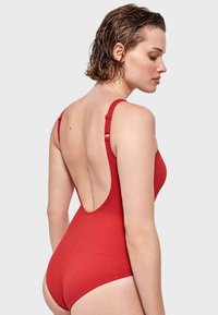 Costume da bagno intero rosso con un motivo testurizzato, spalline larghe e un ampio taglio sulla schiena. Presenta dettagli con spalline regolabili.