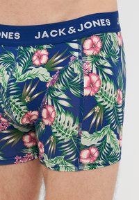 Tengerészeti kék boxer alsónadrág élénk trópusi virágmintával, rózsaszín hibiszkusz virágokkal és zöld levelekkel. Elasztikus derékpánt a márkanevével.