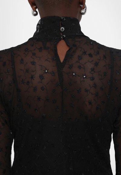 Schwarze transparente Bluse mit floralen Stickereien, hohem Kragen, Knopfverschluss und einem Schlüssellochdetail am Rücken. Textil mit zarten Mustern.