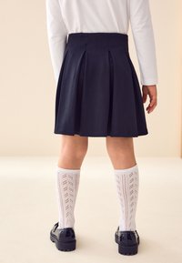 Jupe plissée bleu marine avec une taille ajustée, accompagnée de chaussettes blanches montantes ornées d'un motif décoratif et de chaussures noires.