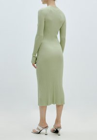 Robe en maille côtelée vert clair à manches longues, coupe ajustée et longueur midi, associée à des talons blancs à lanières avec un bout pointu.