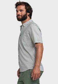 Helles graues Kurzarm-Hemd mit Knöpfen und einer Brusttasche, das eine glatte Textur und subtile Nähedetails aufweist, kombiniert mit grünen Shorts.