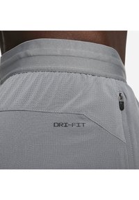 Pantalones cortos atléticos Dri-FIT de color gris claro con un acabado texturizado, que cuentan con un bolsillo con cremallera, cintura elástica y detalles de tela perforada.