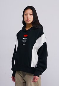 Hoodie Nike noir et blanc avec une poche kangourou, une capuche avec cordon de serrage et un logo sur la poitrine. Tissu doux avec une coupe décontractée.