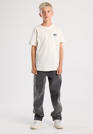 Lichtbeige katoenen t-shirt met korte mouwen en een kleine graphic op de borst, gecombineerd met grijze denim baggy jeans en witte sneakers.