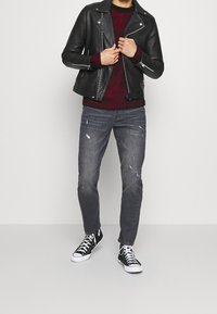 Veste de moto en cuir noir, pull côtelé bordeaux, jean gris usé et baskets noires à semelles blanches. Tenue décontractée en couches.