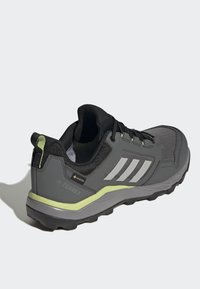 Botte de randonnée grise avec tige en mesh noir, trois rayures blanches et accent vert lime sur la semelle intermédiaire. Possède une semelle texturée et un talon renforcé.