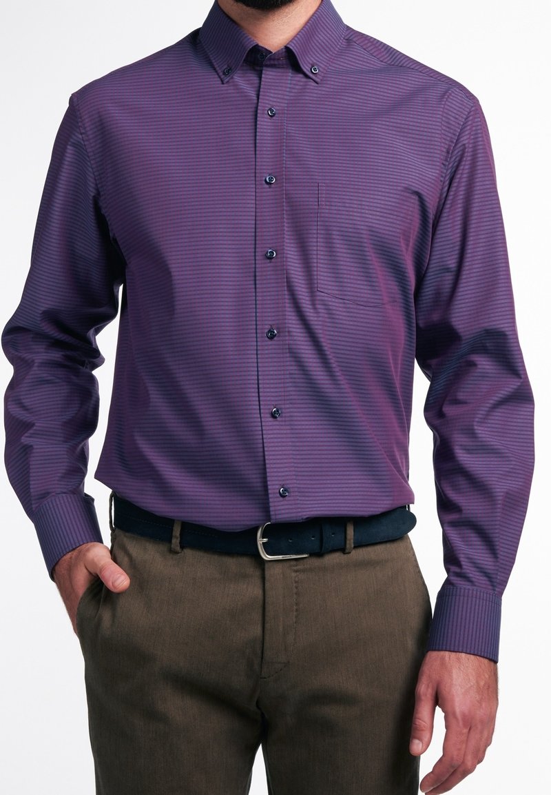 Homme portant une chemise ajustée rayée violette à manches longues avec une poche poitrine et un pantalon marron avec une ceinture noire.