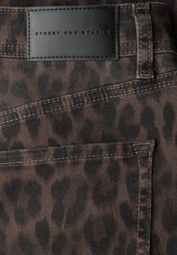 Hnědá denimová látka s černým leopardím vzorem, zdobená černou koženou etiketou s ražbou "STREET ONE STUDIO".