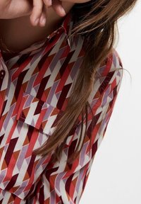 Camicia con un motivo geometrico a diamante in rosso, rosa e crema, dotata di colletto classico e taschino sul petto. Morbido al tatto.