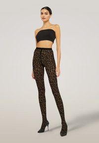 Leggings con stampa leopardata in tessuto trasparente marrone scuro e nero, con una texture liscia, abbinati a un top nero corto e tacchi alti.