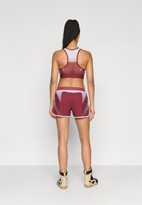 Top desportivo castanho-avermelhado com painéis de rede, combinado com calções castanho-avermelhados coordenados com acabamento branco e detalhes de logótipo. Usado com ténis altos bege.