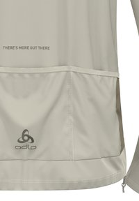 Licht beige sportshirt met een logo en tekst op de bovenrug, een gestructureerde stof en contrasterende kleuraccenten aan de zoom.