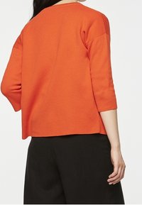 Långärmad, skopa-kant tröja i klargul stickning med avslappnad passform och sänkt axel, matchad med svarta vida byxor.