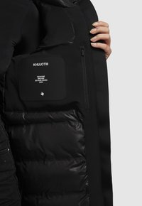 Musta puhvijakku, jossa on sileä pinta ja pehmustettu sisus. Ominaisuuksiin kuuluu merkkilogo, vetoketjullinen tasku ja slim fit -muotoilu.