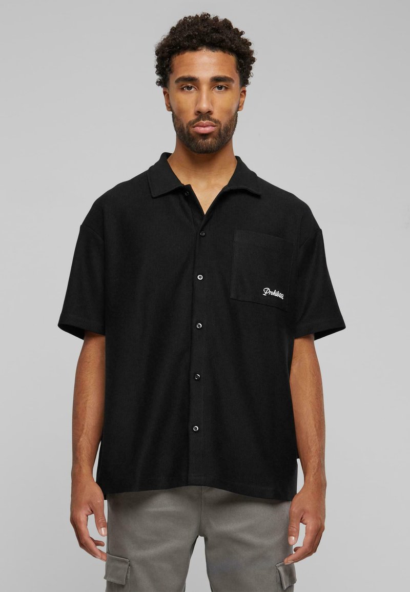 Black short-sleeve shirt made of textured fabric, featuring a collared neckline, front pocket, and logo embroidery on the pocket.