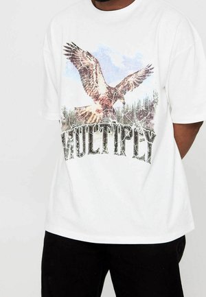 Biały t-shirt z dużą grafiką orła w locie nad drzewami lasu oraz słowem "MULTIPLY" poniżej, napisanym pogrubioną, postarzaną czcionką.