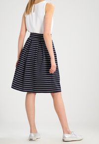 Gonna a righe blu navy e bianche con silhouette svasata, pieghe in vita, abbinata a un top bianco senza maniche e sneakers argento.