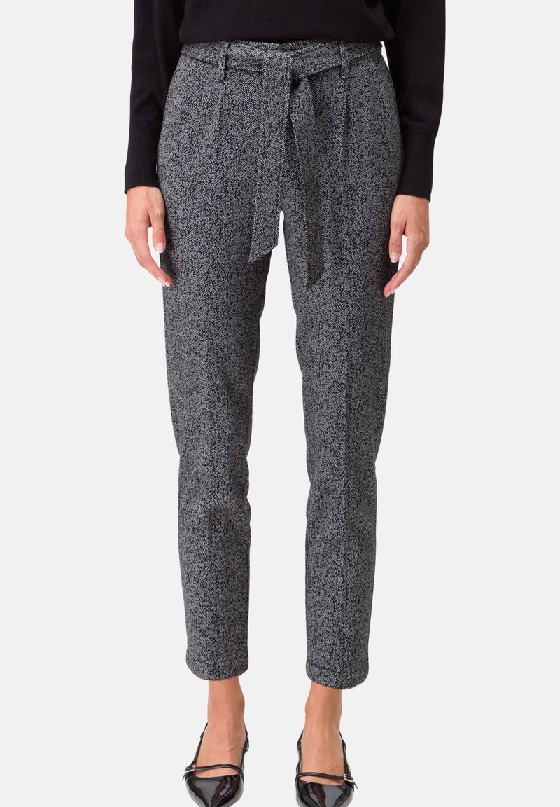 Femme portant un pantalon gris texturé taille haute avec une ceinture nouée à l'avant et des talons noirs, associé à un haut noir à manches longues.
