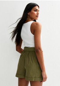 White ribbed tank top paired with olive green linen shorts featuring a drawstring waist and side pockets, shown from a rear angle.