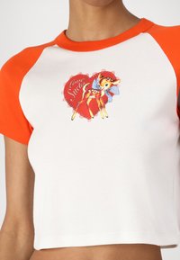 Cropped t-shirt with orange raglan sleeves, white body, and a printed graphic of a fawn with a blue bow on a heart background.