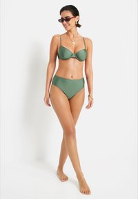 Žalias bikini komplektas, turintis struktūrizuotą, su viela palaikomą viršų su reguliuojamomis petnešomis ir aukštu liemeniu, pagamintas iš lygaus audinio.