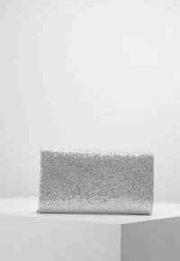 Pochette rectangulaire en argent recouverte d'un tissu en maille métallique brillante, exposée sur un piédestal blanc.
