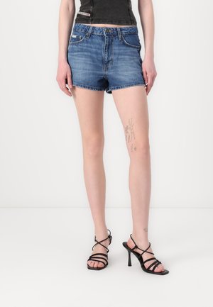Pantalones cortos de mezclilla de color azul claro con dobladillo desgastado, que cuentan con bolsillos delanteros y cierre de botón. Combinados con sandalias negras de tacón alto con tiras.