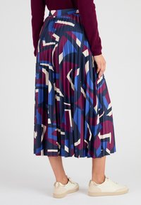 Gonna plissettata blu navy con motivi geometrici in bordeaux, blu e crema. Design a vita alta abbinato a sneaker bianche e dorate.