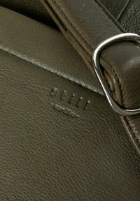 Olivengrøn lædertaske med tekstureret overflade, der har en sølvfarvet metalspænde og præget logo nær sømmen.