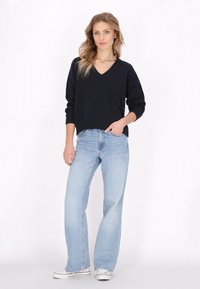 Marineblauw gebreid sweater met een V-hals en lange mouwen, gecombineerd met lichtblauwe high-waisted wijde jeans en witte sneakers.