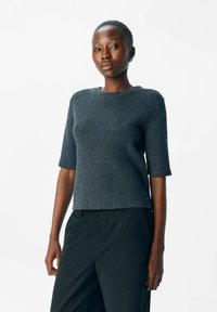 Dunkelgrauer gerippter Strickpullover mit kurzen Ärmeln und Rundhalsausschnitt, gerade geschnitten und mit strukturiertem Stoff. Getragen mit schwarzen Hosen.