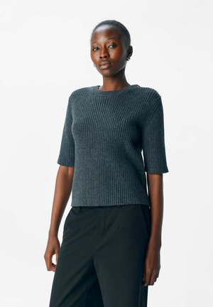 Pull en maille côtelée gris foncé à manches courtes et col rond, avec une coupe droite et un tissu texturé. Porté avec un pantalon noir.